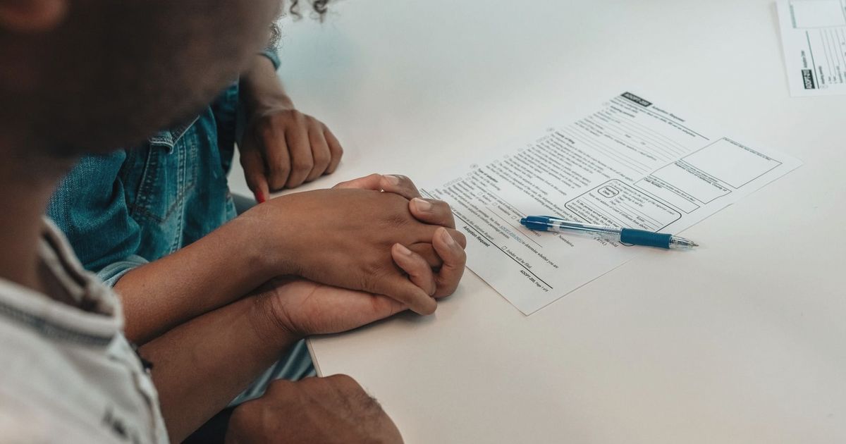 A family supports each other during an adoption process, holding hands over important documents.