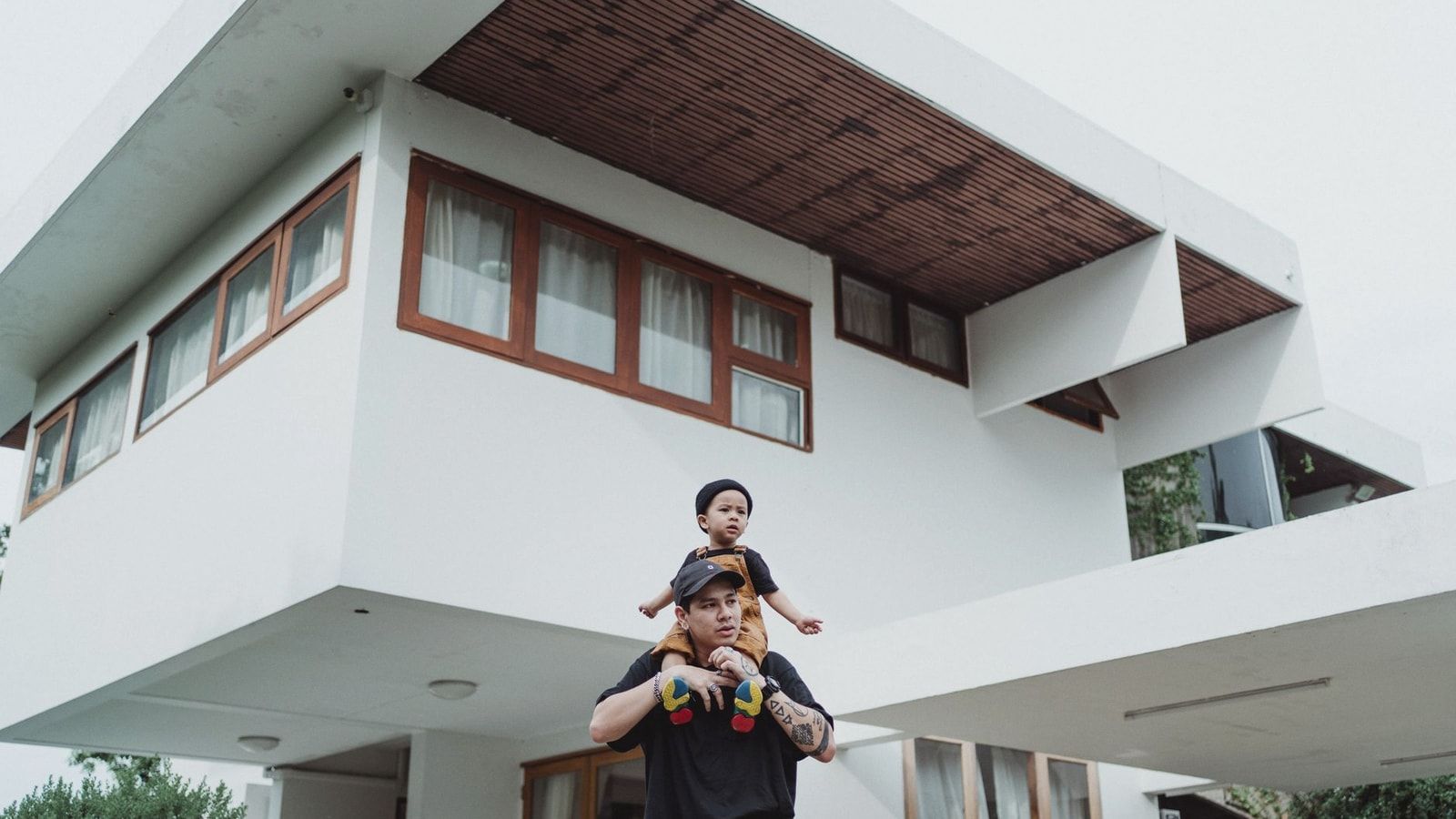 Father and son bonding on a piggyback ride in front of a modern house with unique architecture.