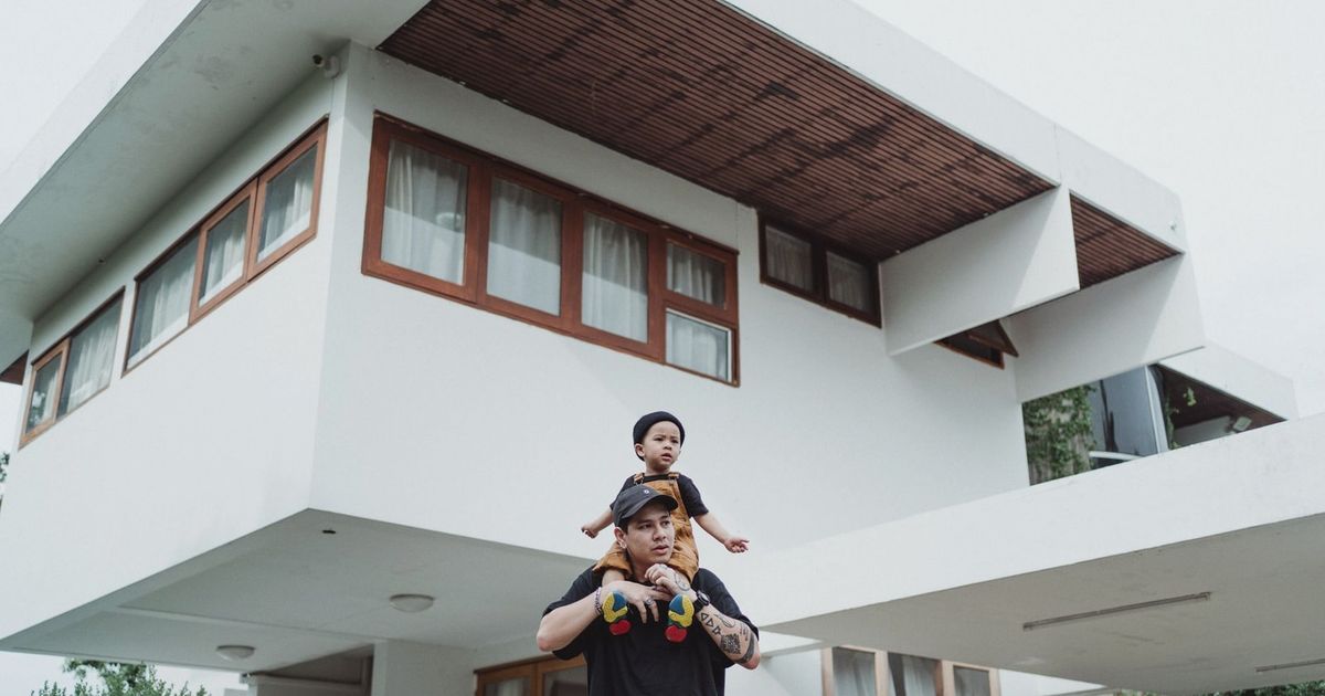 Father and son bonding on a piggyback ride in front of a modern house with unique architecture.