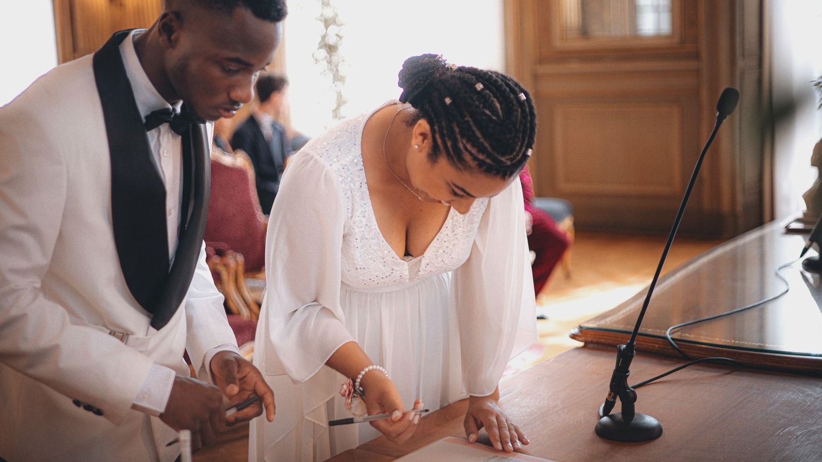Bride and groom signing documents at a formal indoor wedding ceremony.