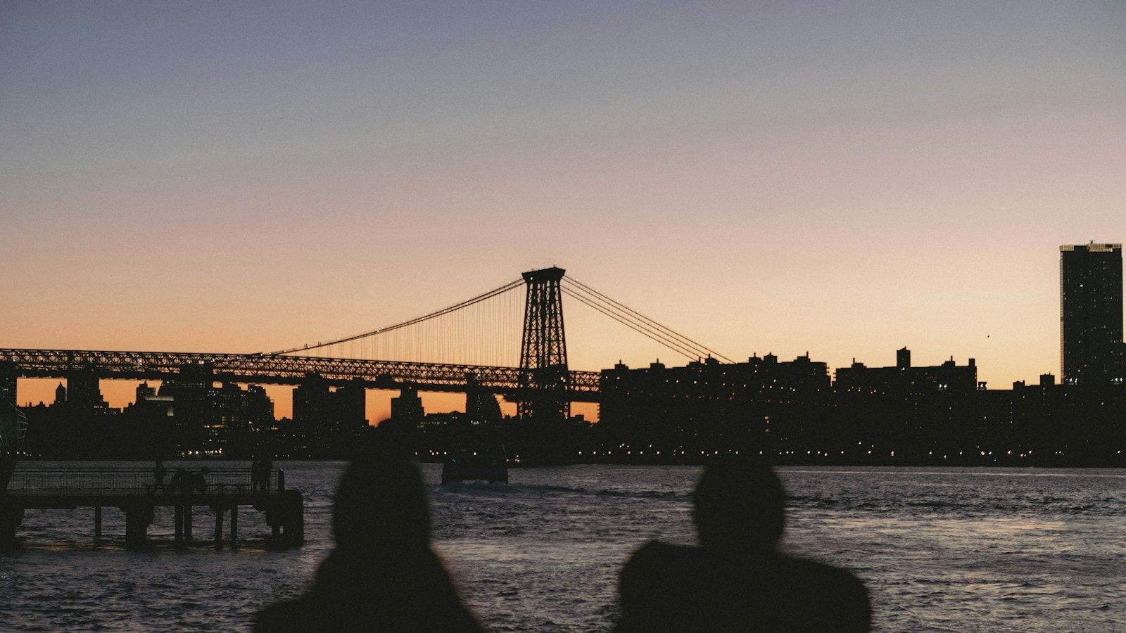 two people sitting on a bench looking at a bridge