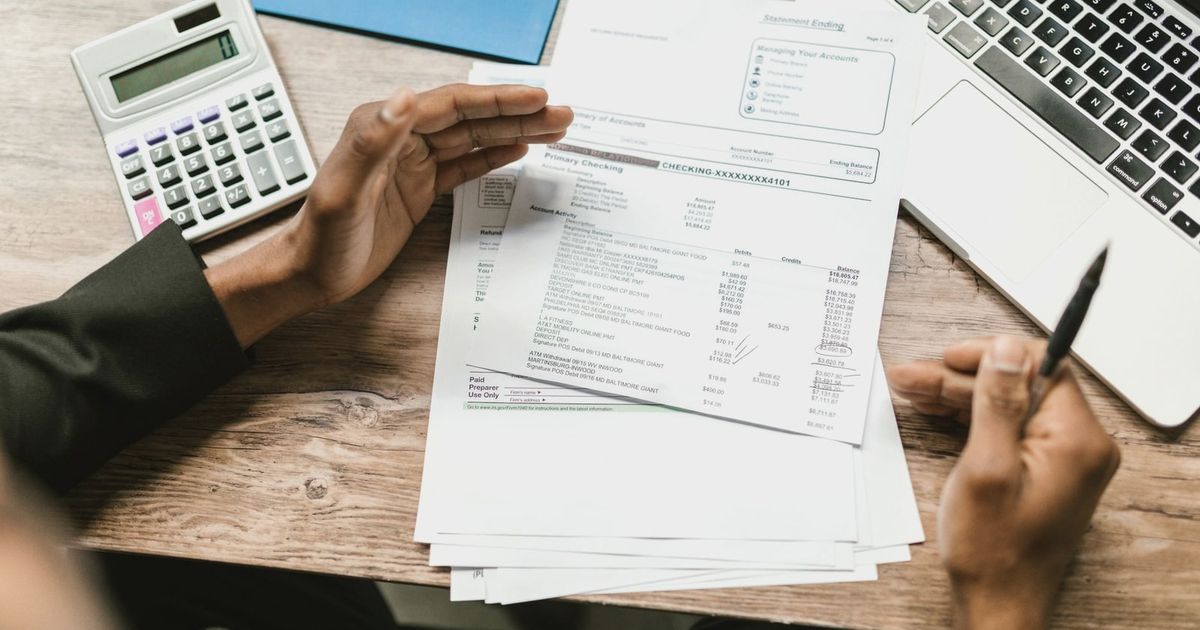 Hands holding financial documents with calculator and laptop on office desk, business analysis scene.