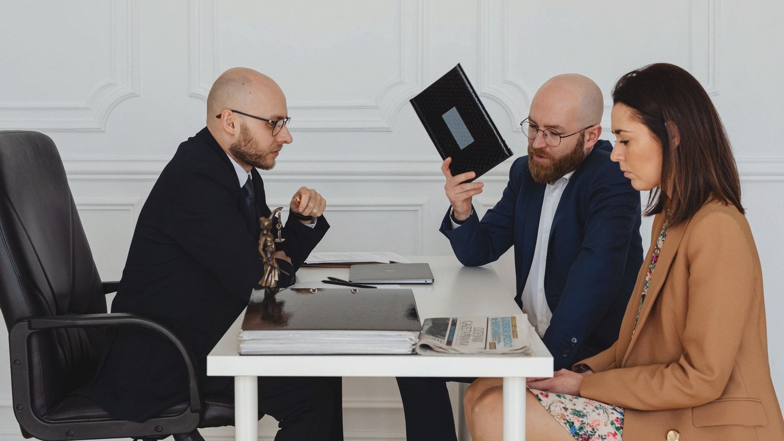 A couple in a legal consultation with a lawyer at an office desk.