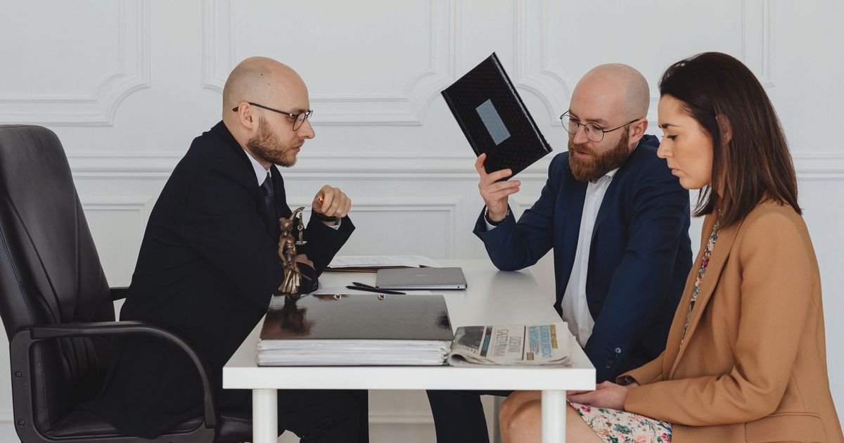 A couple in a legal consultation with a lawyer at an office desk.