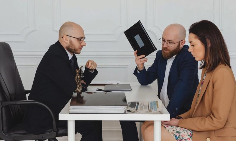 A couple in a legal consultation with a lawyer at an office desk.