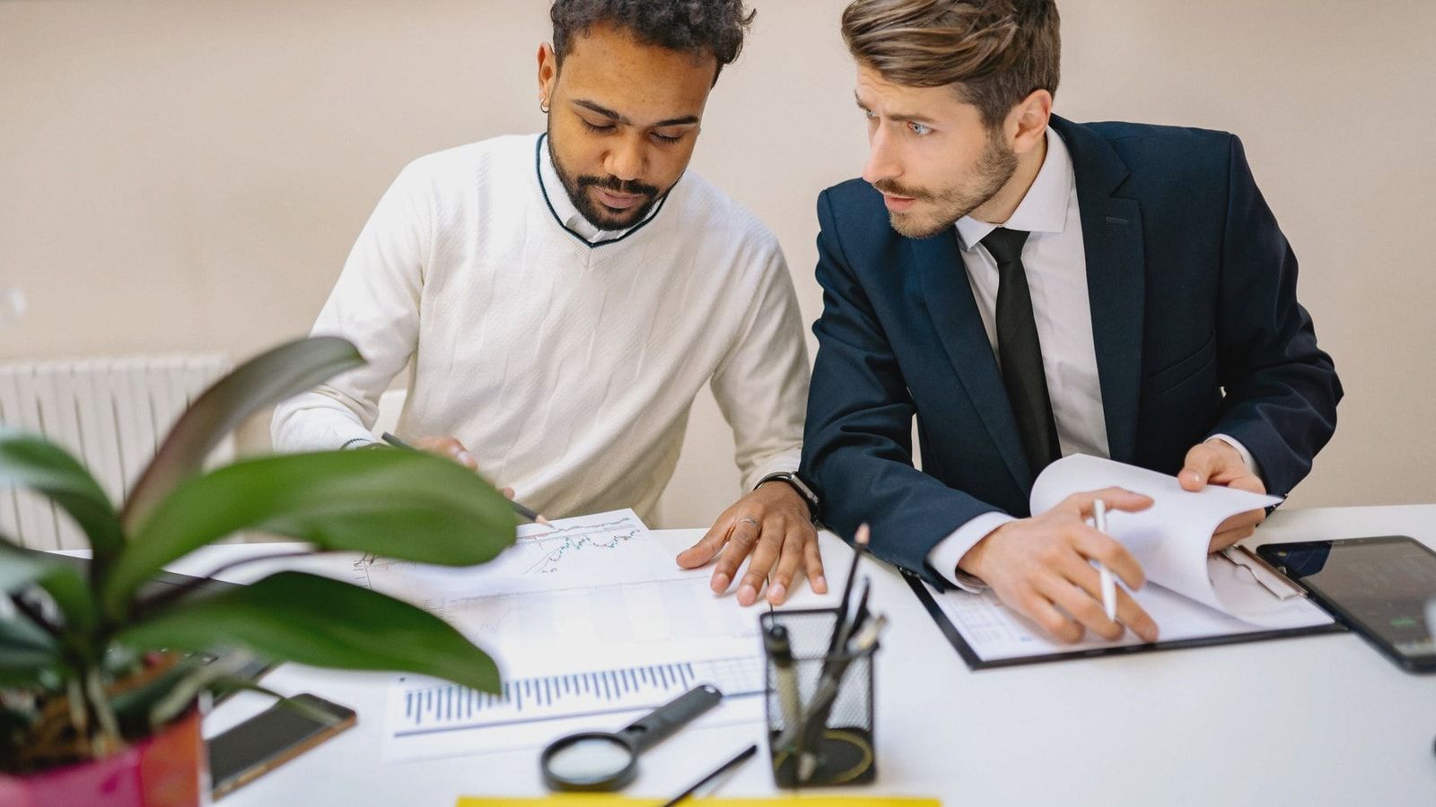 Two men in a modern office discussing and analyzing documents with charts.