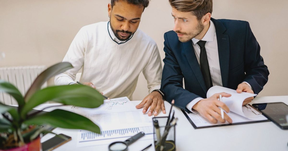 Two men in a modern office discussing and analyzing documents with charts.