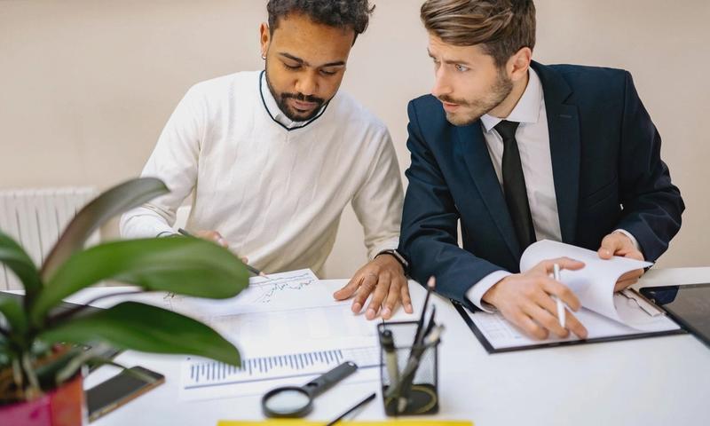 Two men in a modern office discussing and analyzing documents with charts.