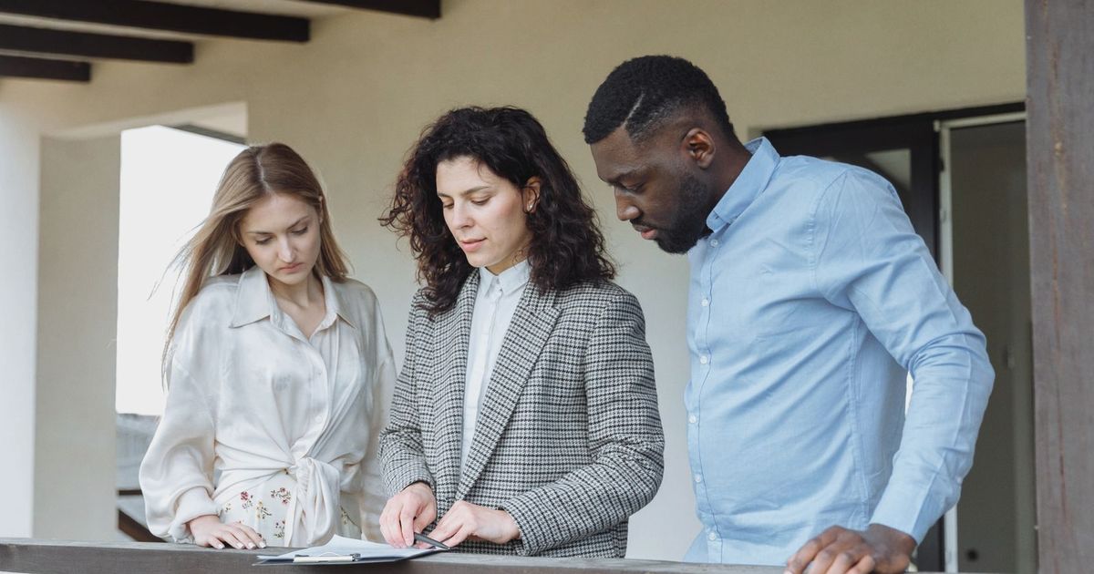 Three adults reviewing documents on a balcony during a real estate consultation.