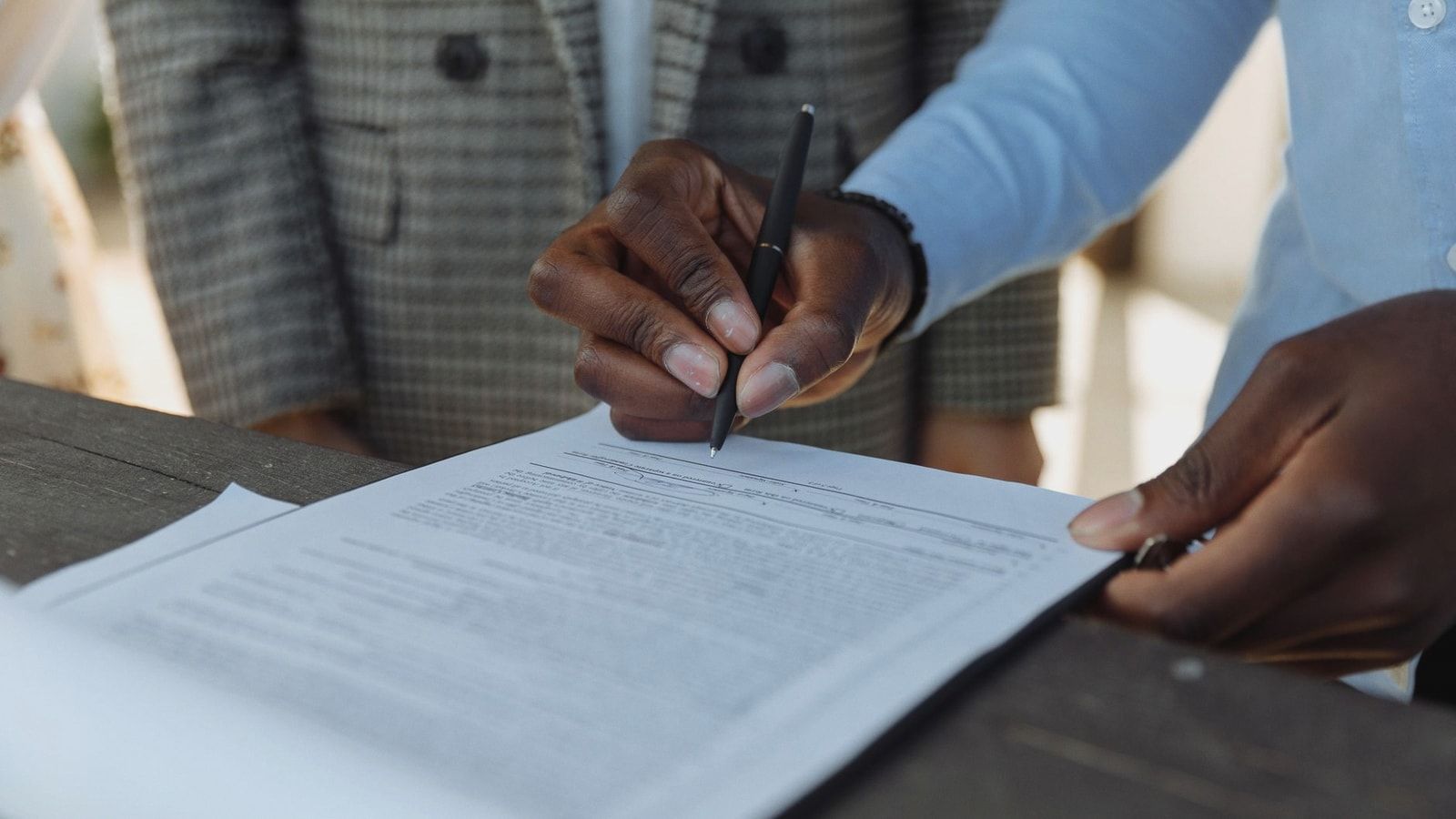 Close-up of business professionals signing a document with a pen indoors.
