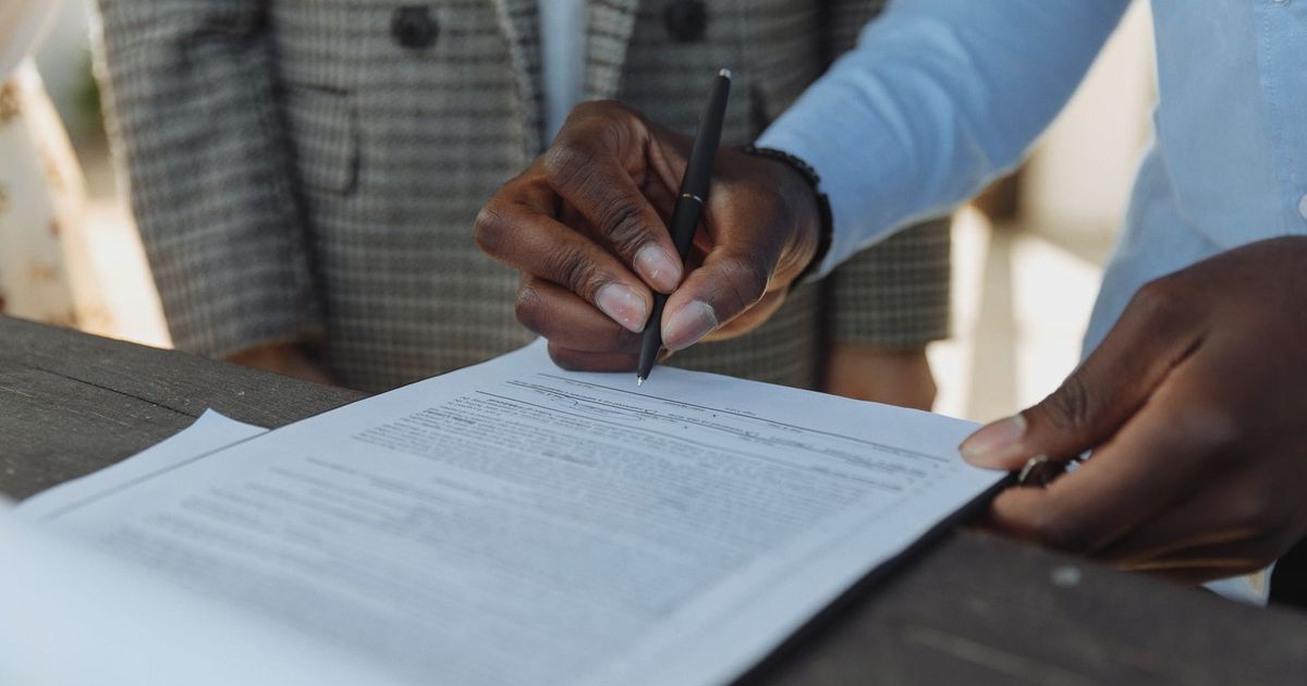 Close-up of business professionals signing a document with a pen indoors.