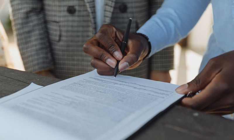 Close-up of business professionals signing a document with a pen indoors.