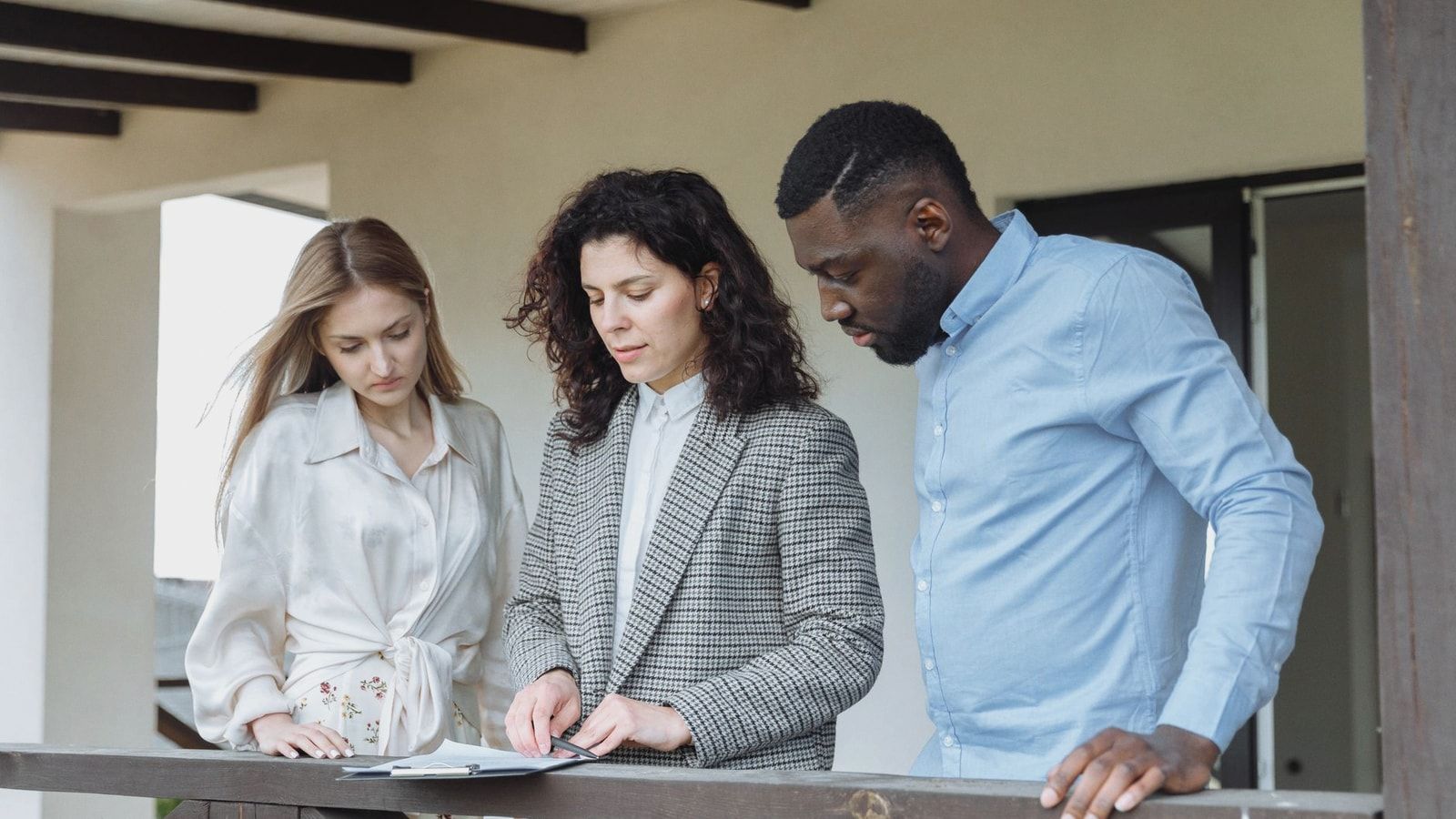Three adults reviewing documents on a balcony during a real estate consultation.