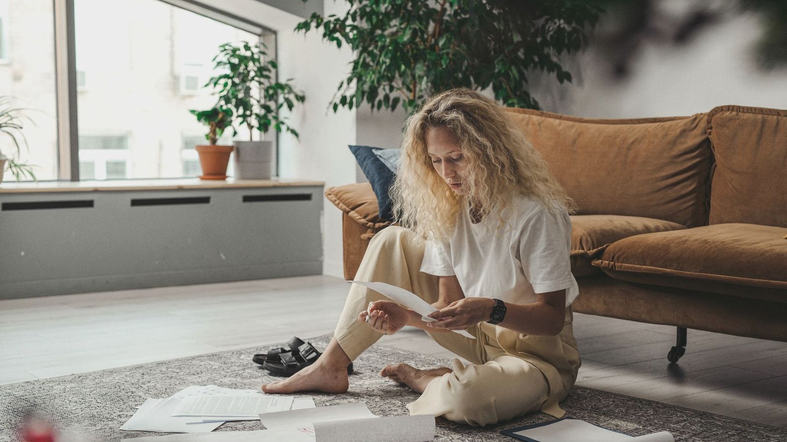 Woman sitting on the floor at home, reviewing paperwork in a relaxed environment.