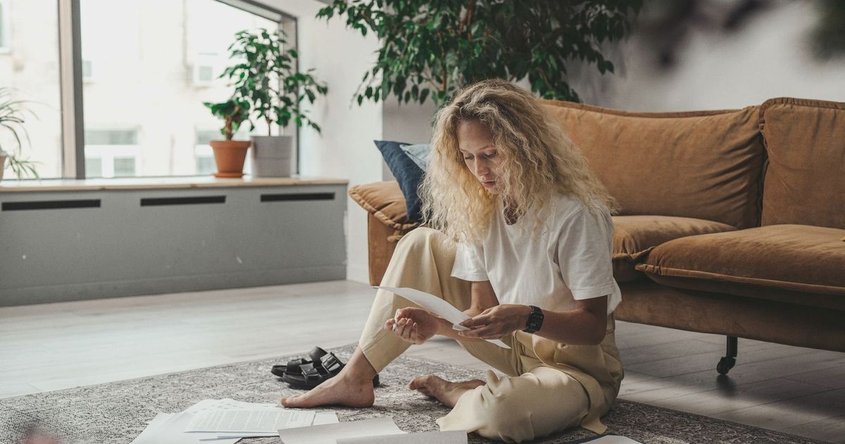 Woman sitting on the floor at home, reviewing paperwork in a relaxed environment.