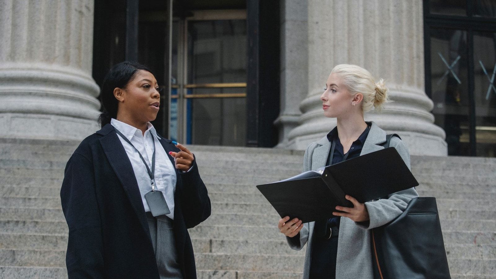 Smart young multiracial female lawyers talking about case standing near aged court building with columns before trial