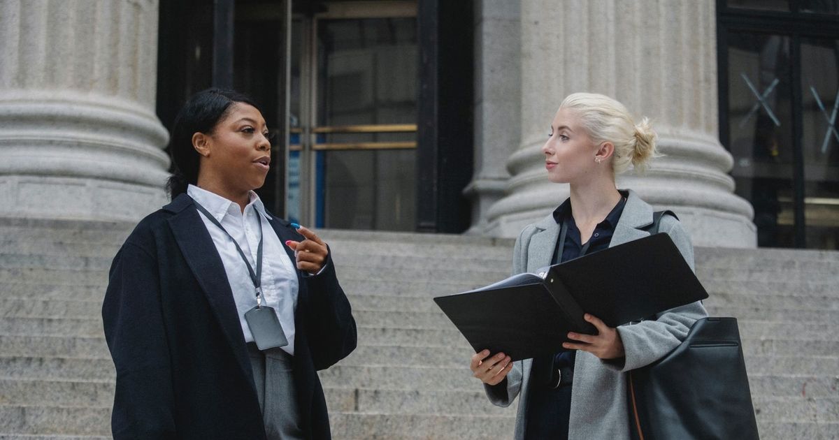 Smart young multiracial female lawyers talking about case standing near aged court building with columns before trial