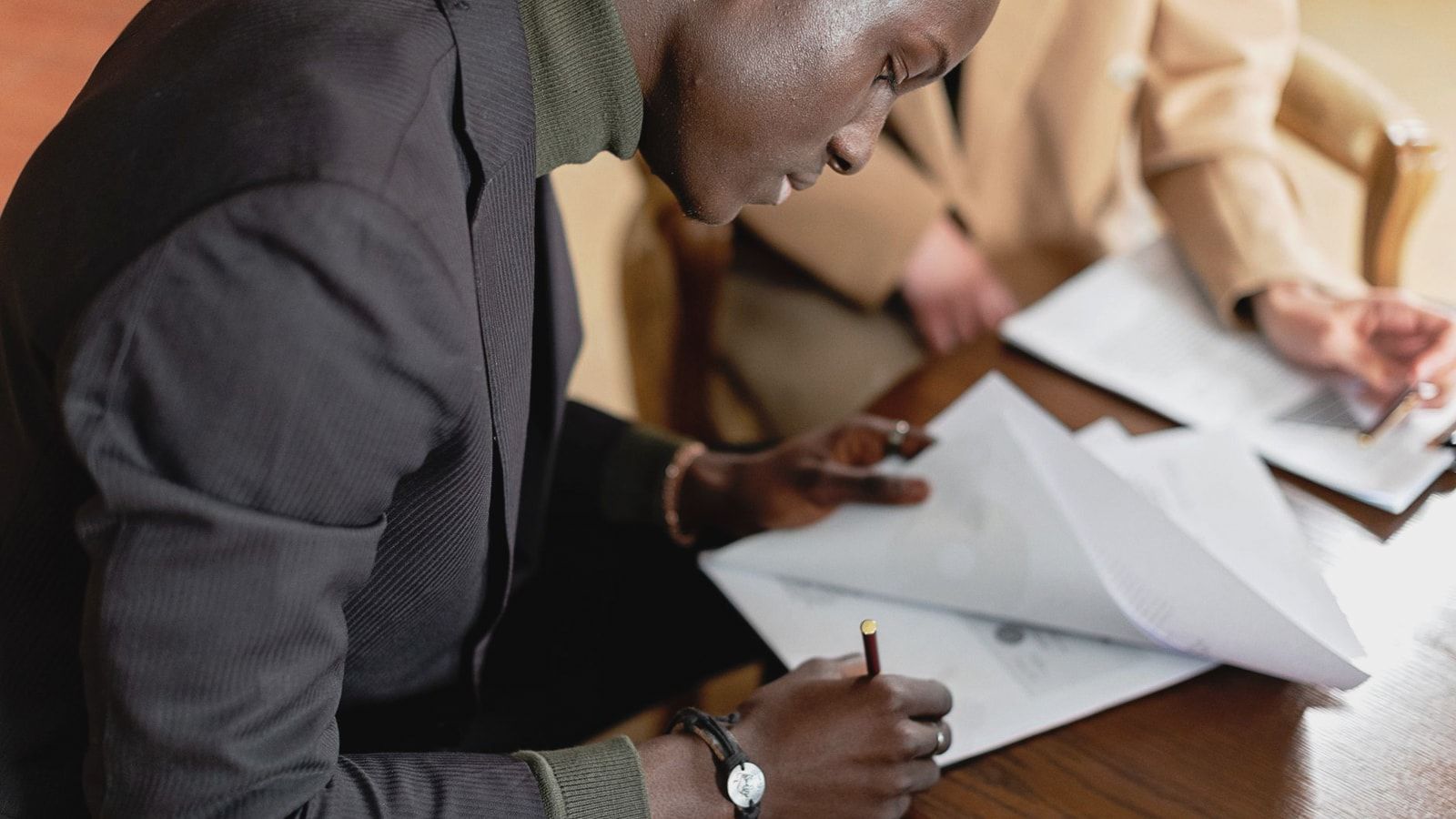 African American man focused on signing important business documents at a desk.