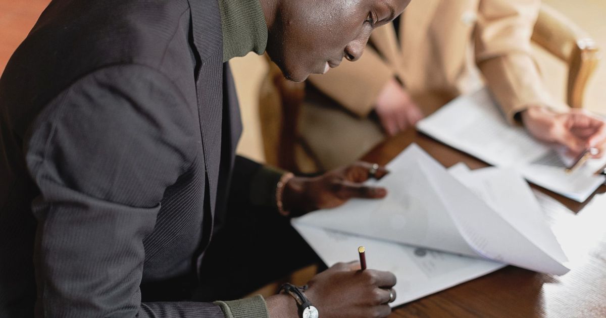 African American man focused on signing important business documents at a desk.