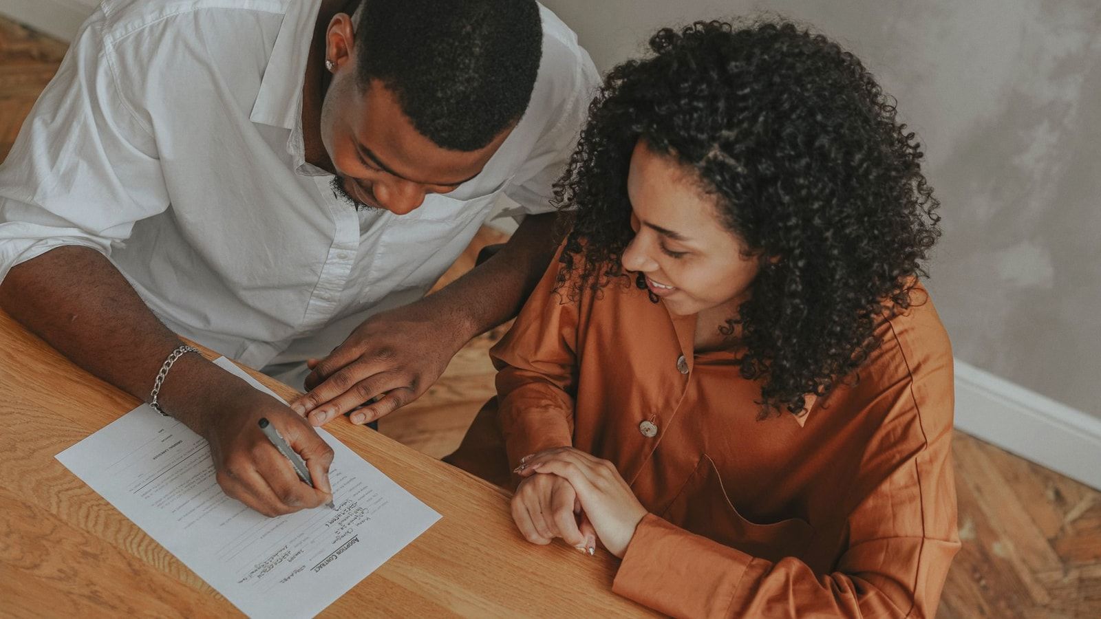 A couple signing an adoption certificate at a table, viewed from above.
