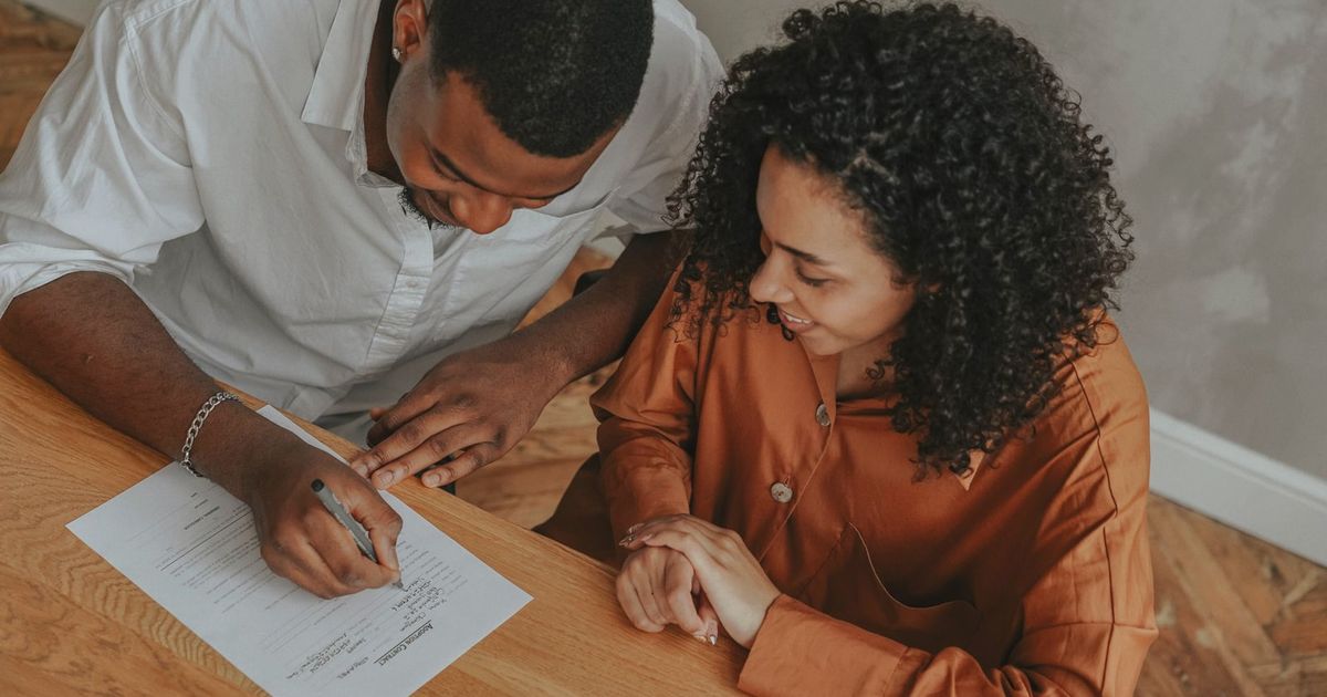 A couple signing an adoption certificate at a table, viewed from above.