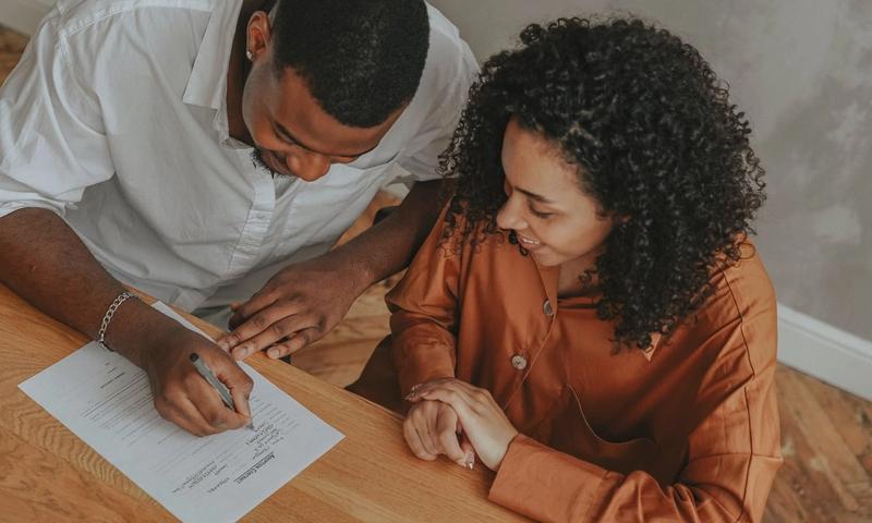A couple signing an adoption certificate at a table, viewed from above.