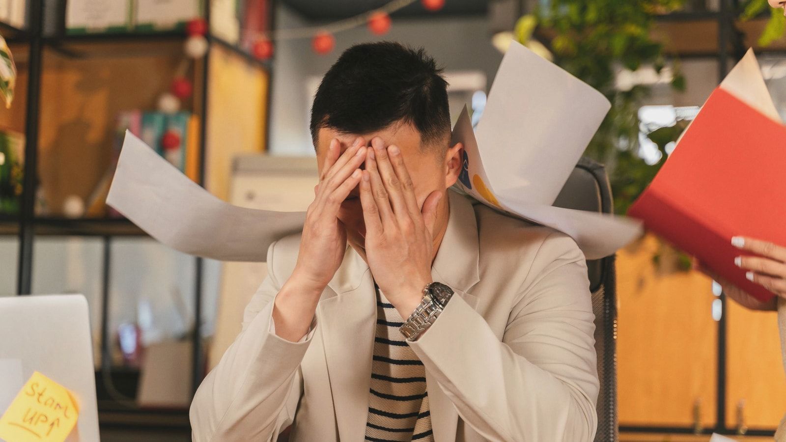 Stressed businessman overwhelmed by paperwork in office environment, demonstrating burnout.