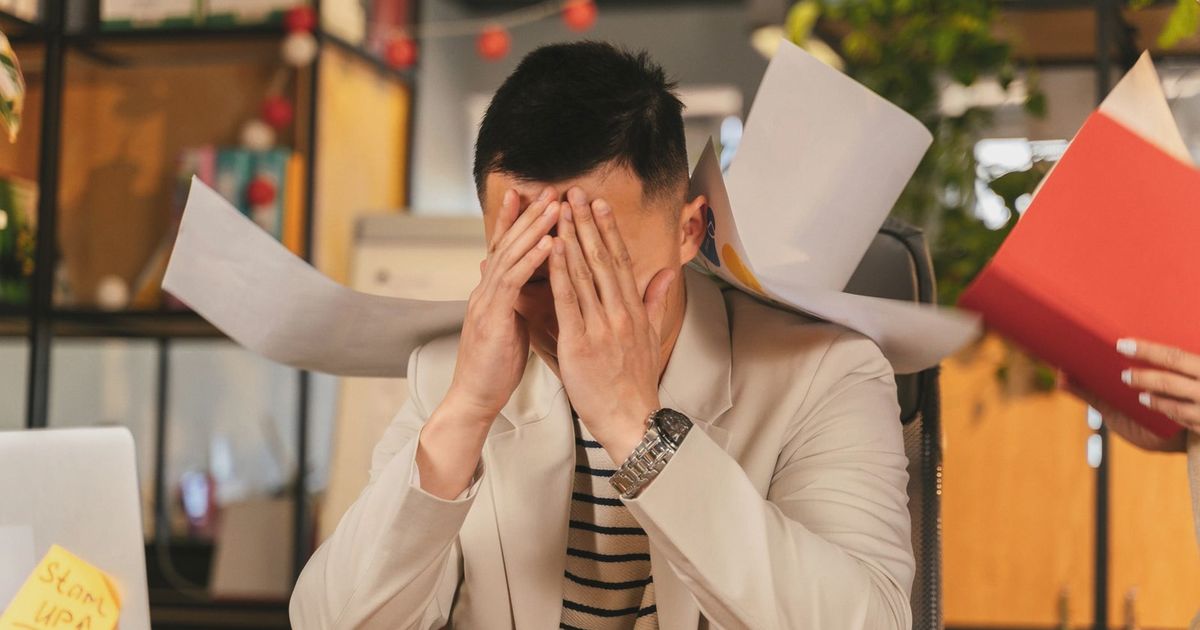 Stressed businessman overwhelmed by paperwork in office environment, demonstrating burnout.