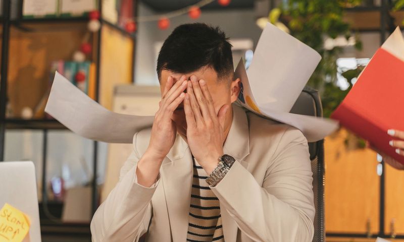 Stressed businessman overwhelmed by paperwork in office environment, demonstrating burnout.
