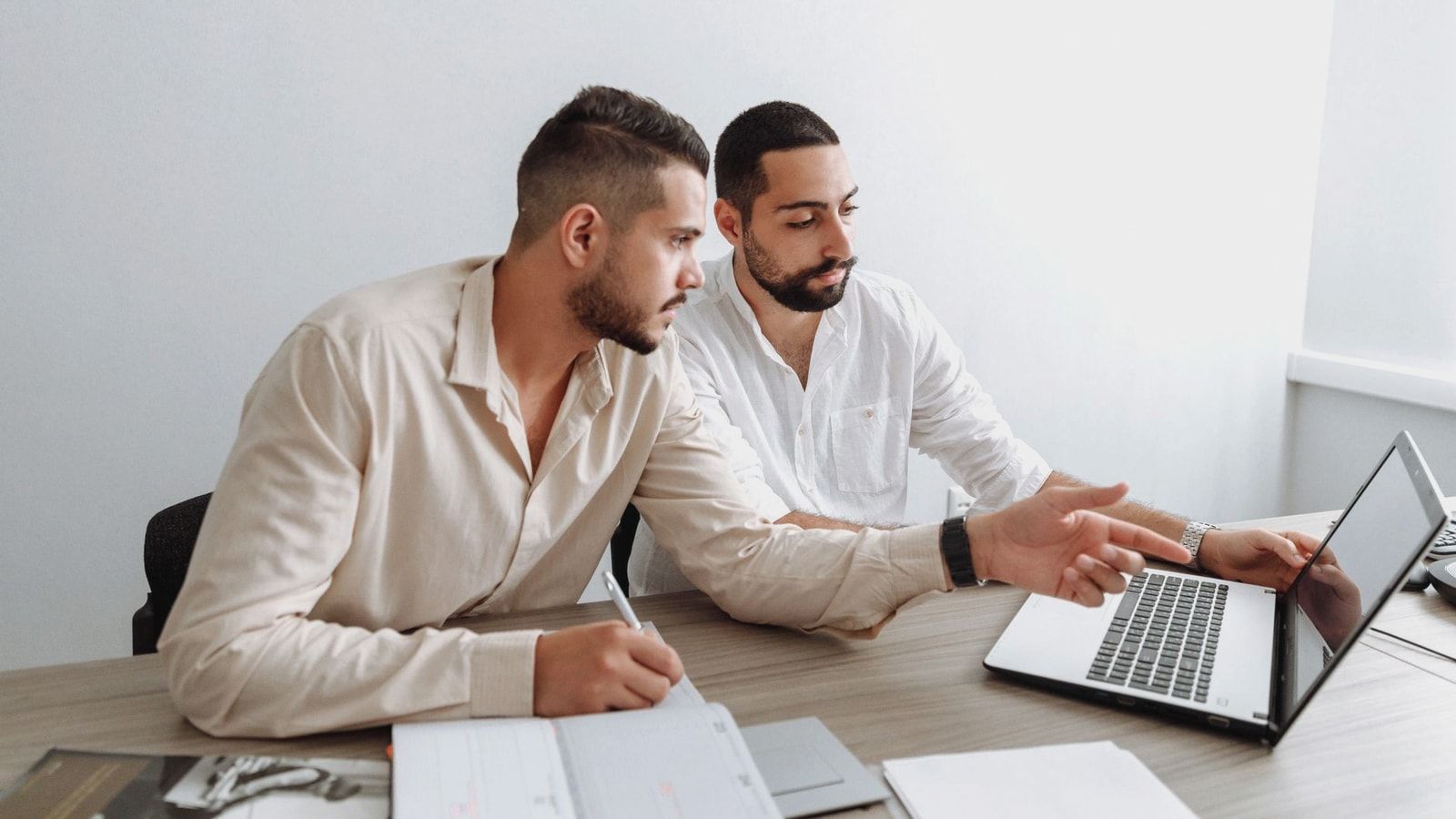 Two men working together on a laptop during a business meeting indoors.