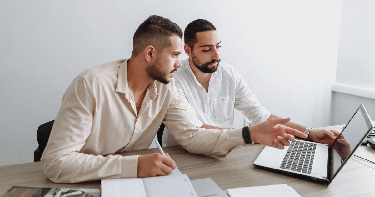 Two men working together on a laptop during a business meeting indoors.