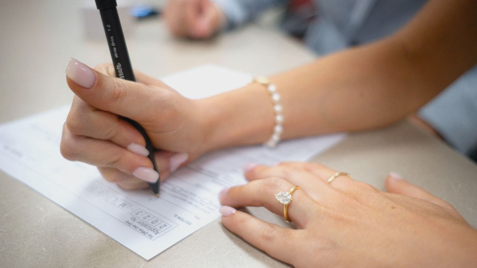 Detailed view of hands filling out a form with elegant jewelry and manicure.