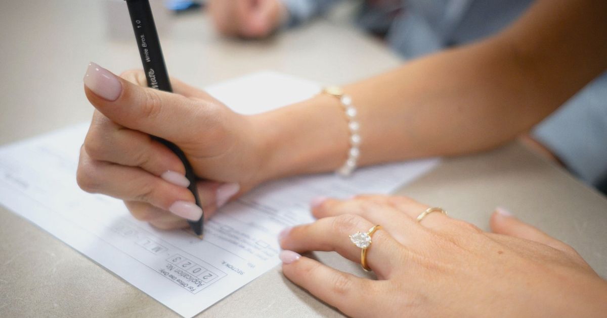 Detailed view of hands filling out a form with elegant jewelry and manicure.