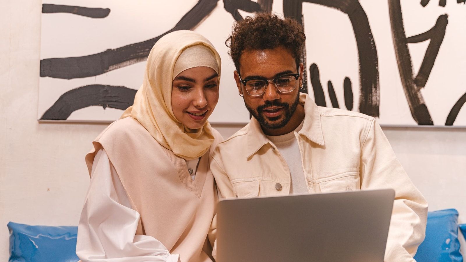 A young Muslim couple in stylish attire collaborating on a laptop indoors.
