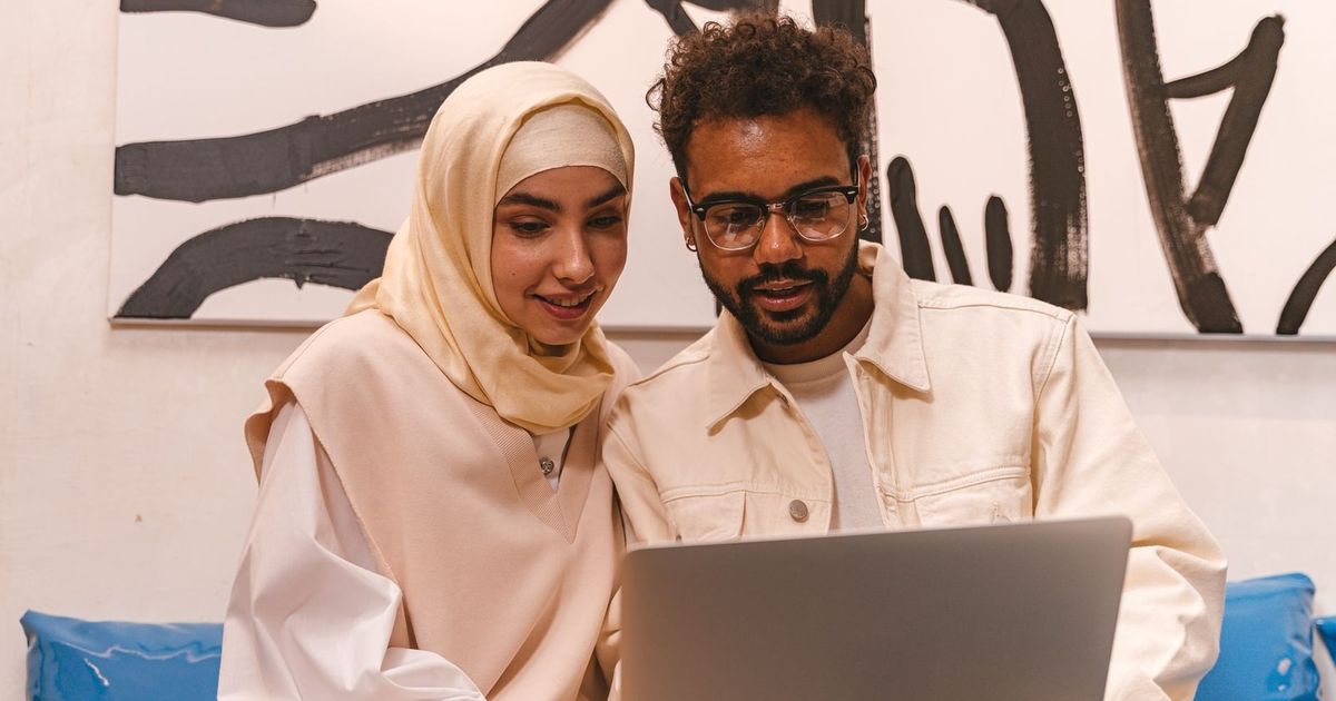 A young Muslim couple in stylish attire collaborating on a laptop indoors.