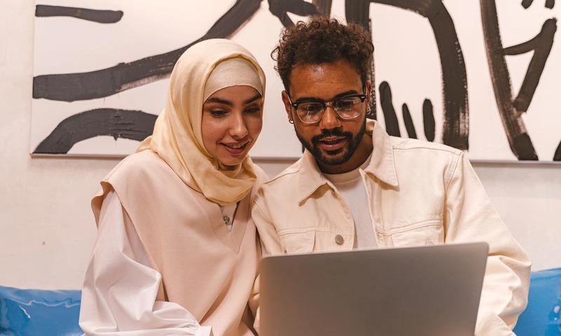 A young Muslim couple in stylish attire collaborating on a laptop indoors.