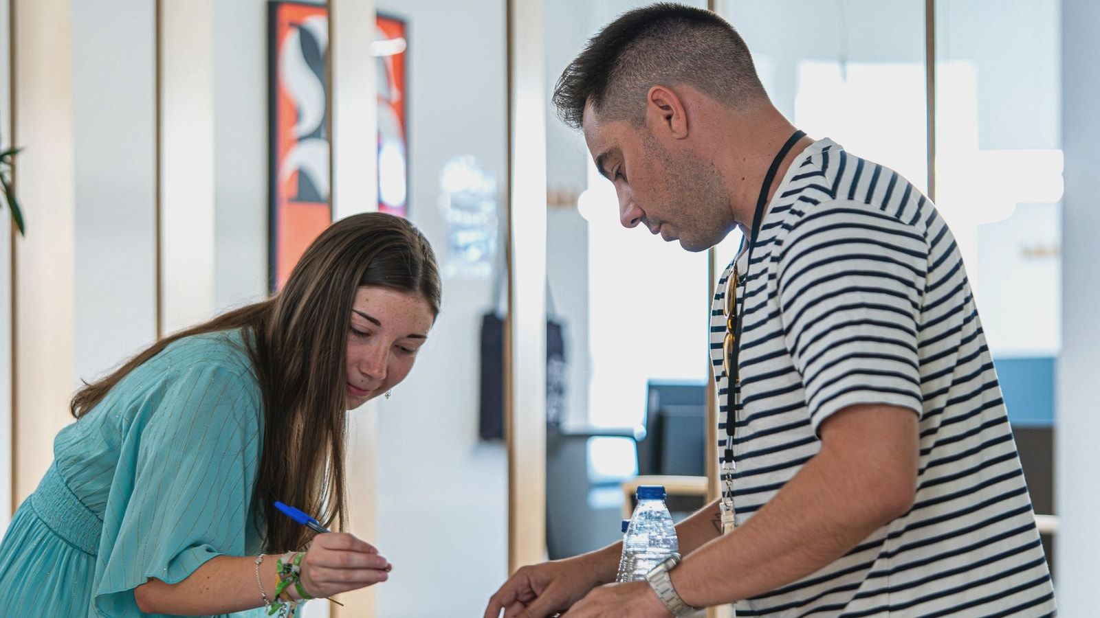 Two young adults working together in a contemporary office setting, discussing and signing documents.