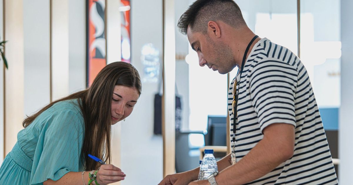 Two young adults working together in a contemporary office setting, discussing and signing documents.