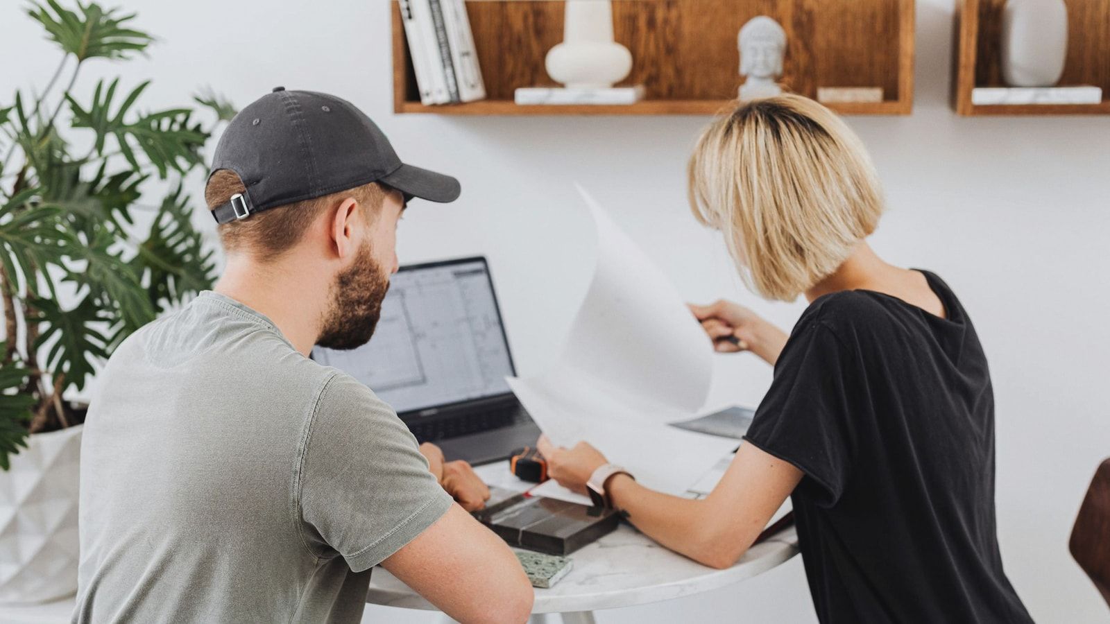Two coworkers collaborating in a modern office setting, reviewing documents over a laptop.