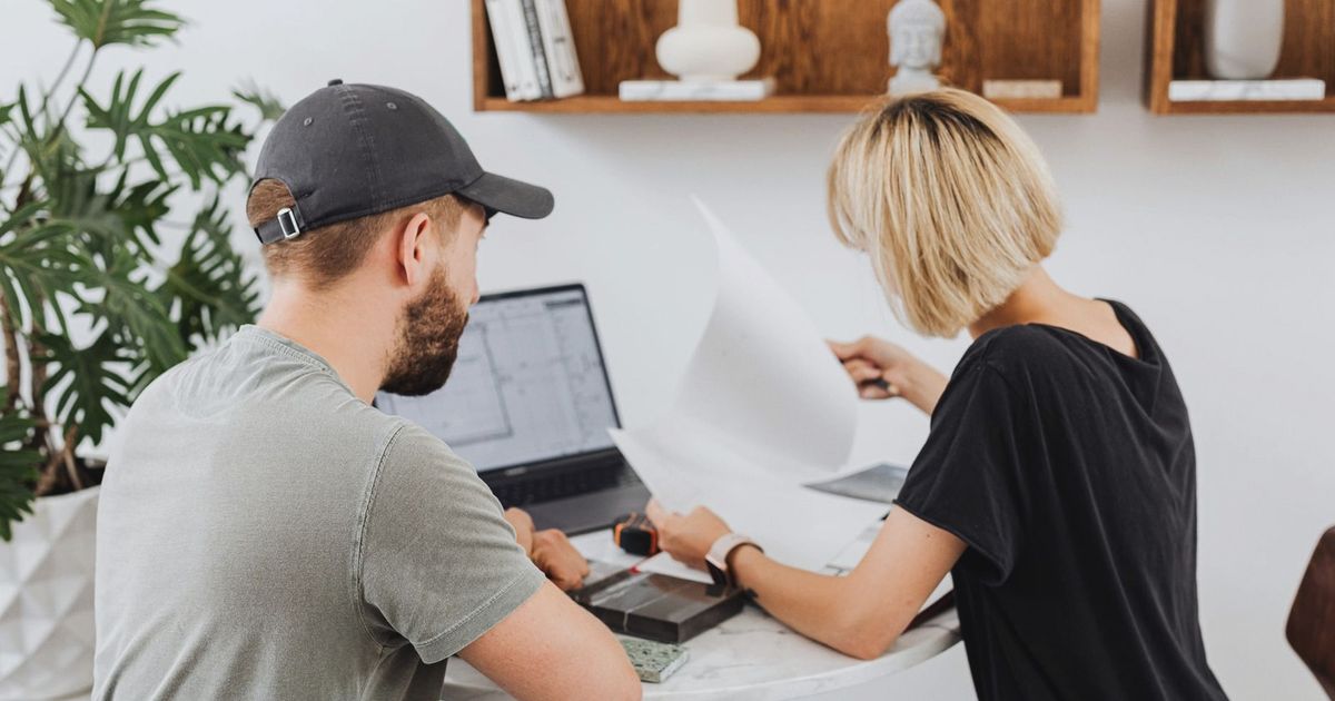 Two coworkers collaborating in a modern office setting, reviewing documents over a laptop.
