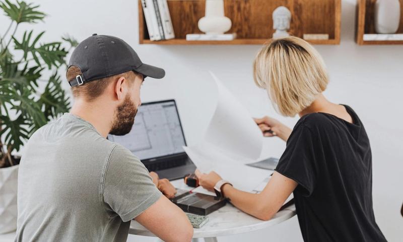 Two coworkers collaborating in a modern office setting, reviewing documents over a laptop.