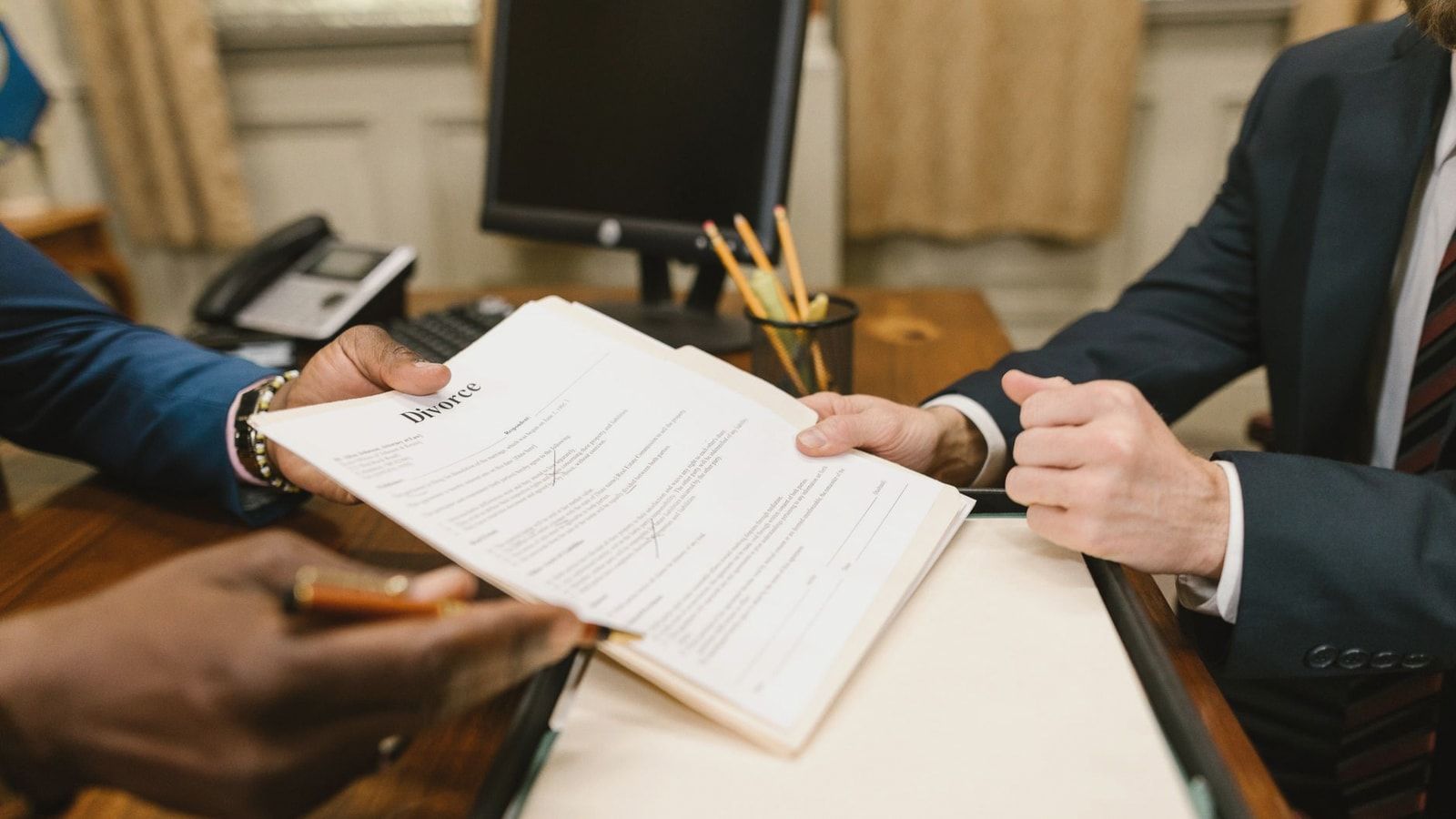 Close-up of hands exchanging divorce documents during legal proceedings in office.