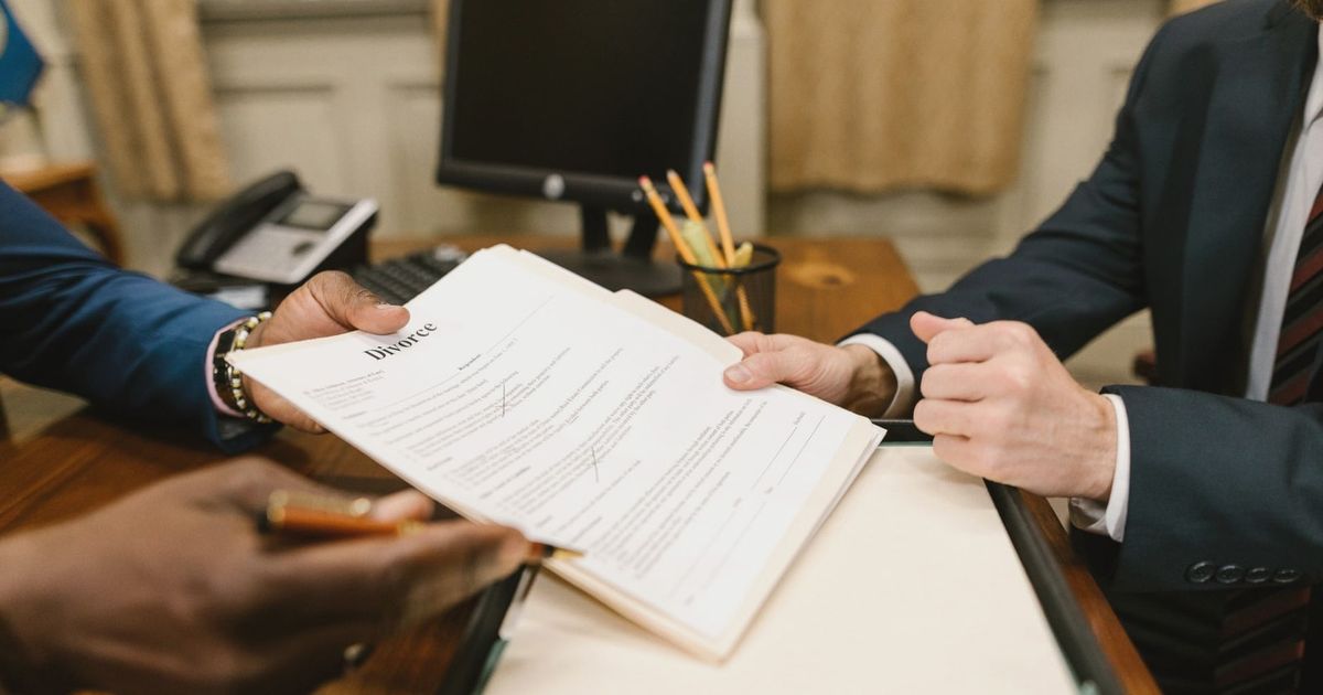 Close-up of hands exchanging divorce documents during legal proceedings in office.