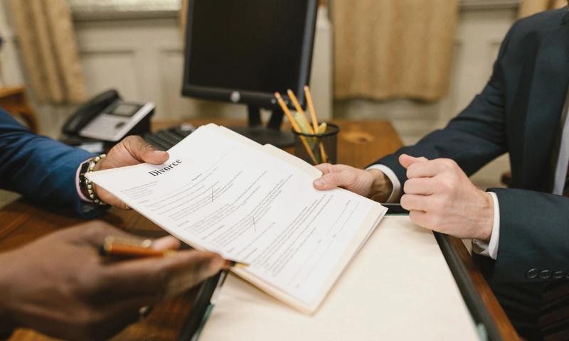 Close-up of hands exchanging divorce documents during legal proceedings in office.