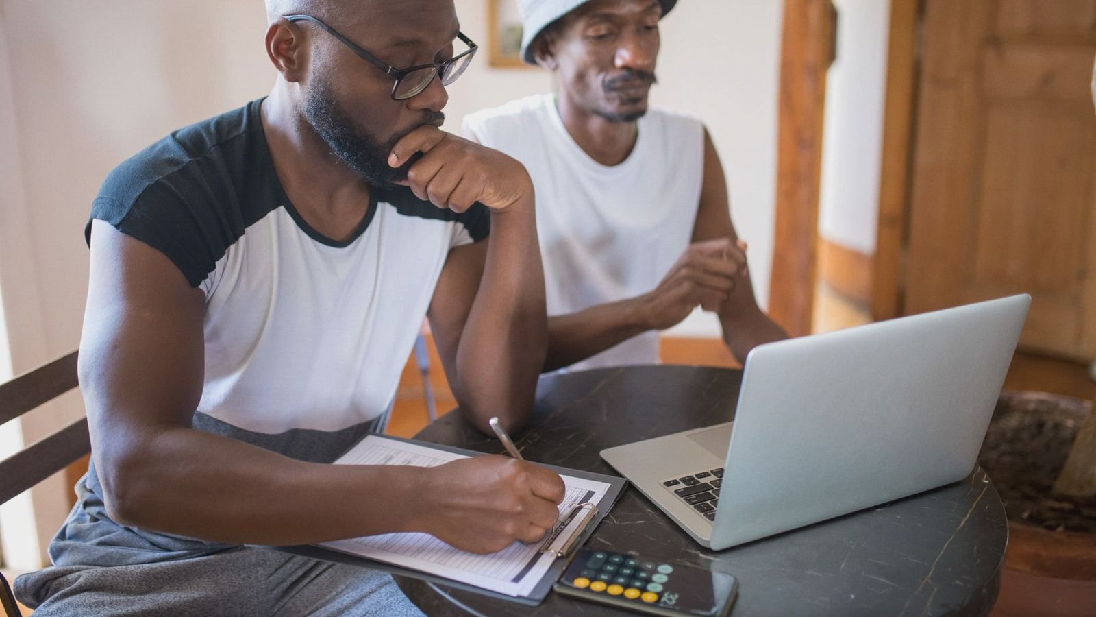 Two men working together at home with a laptop and documents, focusing on collaboration.