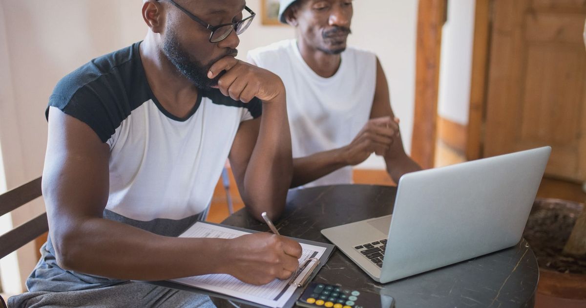 Two men working together at home with a laptop and documents, focusing on collaboration.