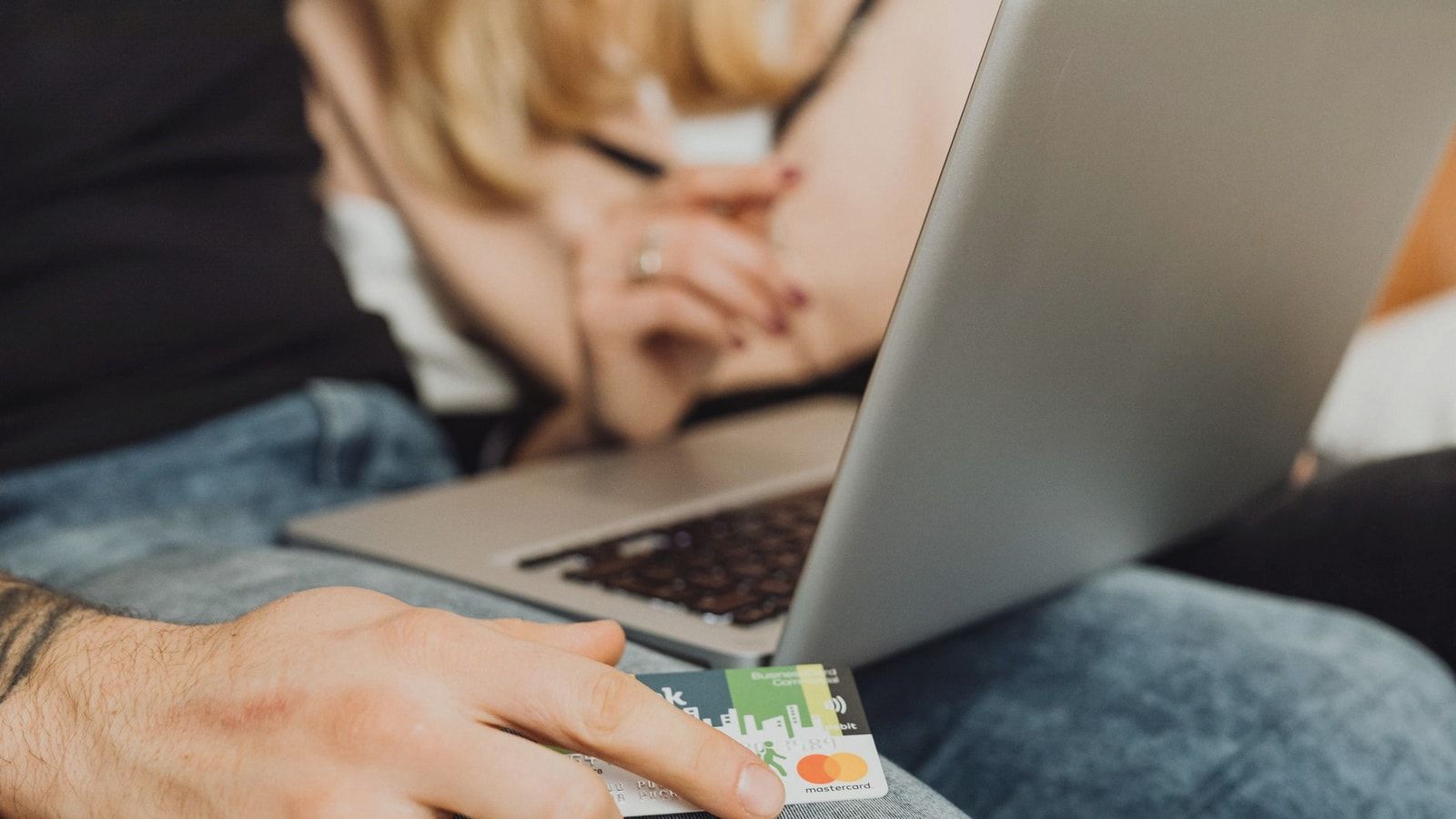 A couple using a laptop for online shopping, holding a credit card in a cozy setting.