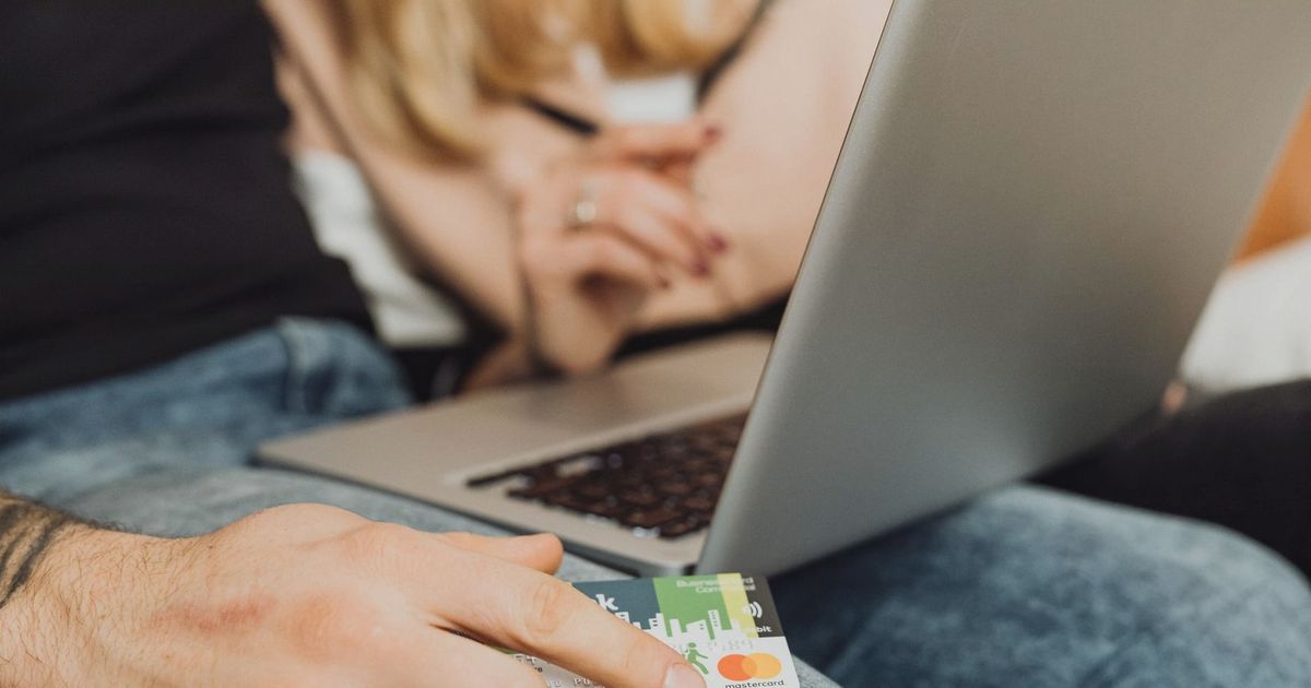 A couple using a laptop for online shopping, holding a credit card in a cozy setting.