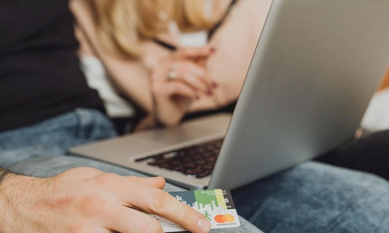 A couple using a laptop for online shopping, holding a credit card in a cozy setting.