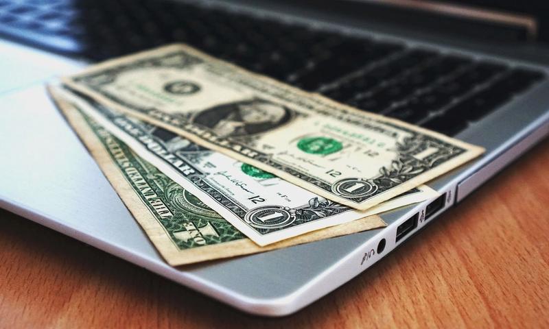 Close-up of US dollar bills placed on a laptop symbolizing digital finance and economy.